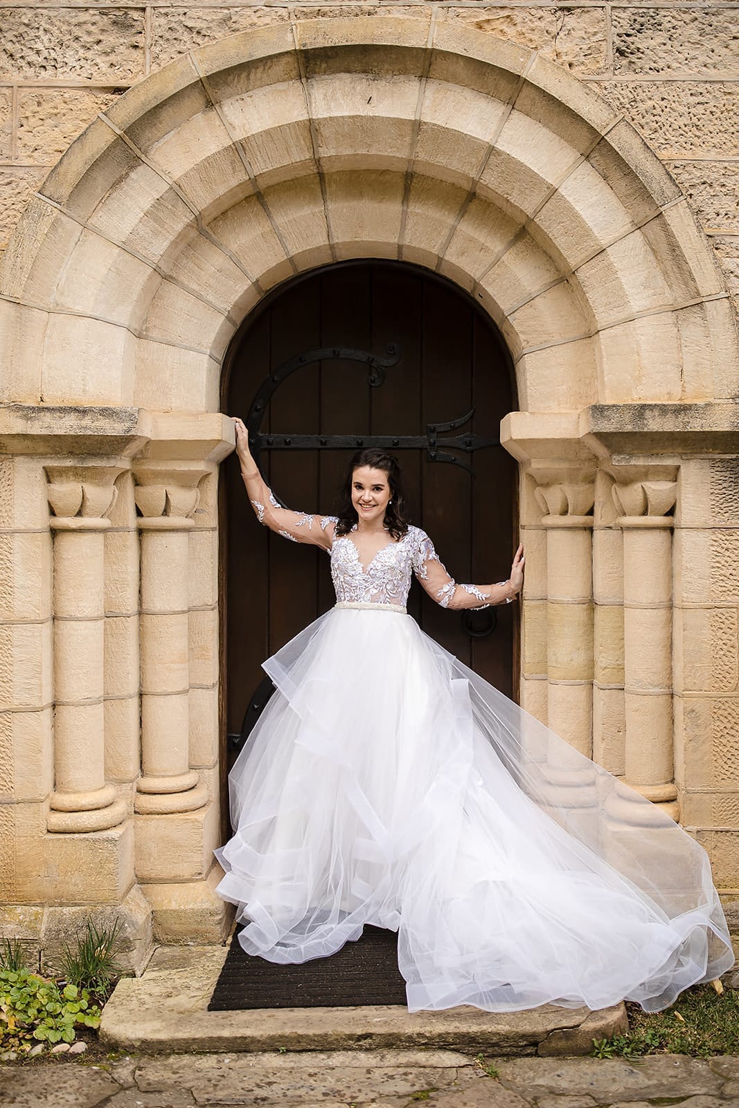 MELINDA Off-White Lace & Tulle Ball Gown  The Melinda bridal gown is a dreamy, ethereal creation designed for the bride who envisions a fairy-tale wedding. Crafted from delicate lace and soft tulle, this gown exudes romance and timeless elegance.  The sheer lace bodice is adorned with intricate detailing, extending into long, fitted lace sleeves that add a touch of sophistication. The low, open back enhances the design with a modern, alluring twist, offering a perfect balance of grace and contemporary style.  The voluminous ball gown skirt is crafted from layers of soft tulle, cascading into graceful, ruffled tiers. Each tier is finished with horsehair hems, adding structure, movement, and a whimsical, flowing effect as the bride glides down the aisle.