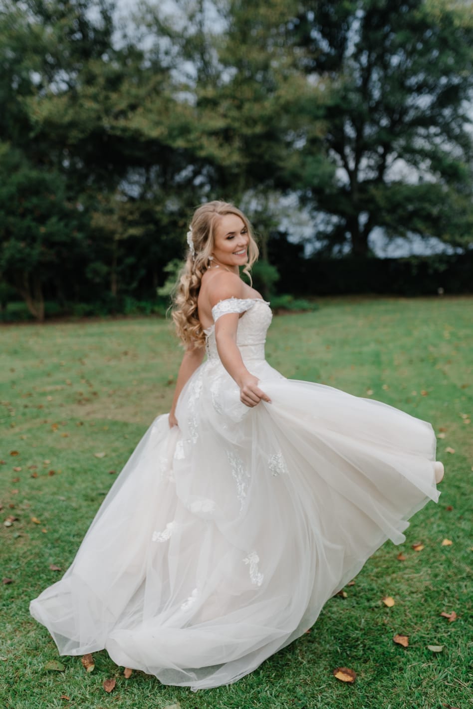 HAILEY A dreamy blush wedding gown, designed with shimmering tulle and delicate lace in a soft blush hue. The strapless sweetheart neckline beautifully frames the décolletage, while the bodice is adorned with intricate floral lace appliqués that add texture and romance. The A-line tulle skirt cascades gracefully, embellished with floral lace details that create a stunning, whimsical effect. Detachable draped tulle sleeves offer a versatile touch, allowing the bride to switch between a classic strapless look and an effortlessly romantic style. This gown captures the perfect balance of elegance and modern bridal charm.