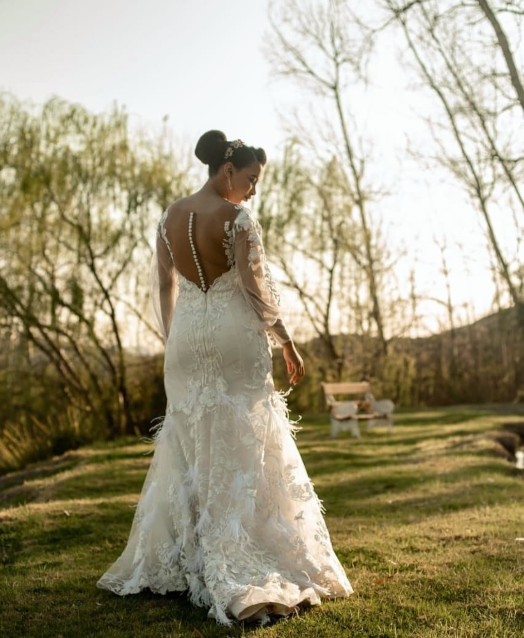 salome Lace Mermaid Gown with Sheer Bateau Neckline and Feather Detail  The Salome gown is a captivating fusion of bold glamour and soft romance. Designed for the bride who desires sophistication with a hint of drama, this lace mermaid silhouette features delicate layering, intricate detailing, and graceful textures that move with you.  ✨ Design Highlights: ✔ Sweetheart Bodice with Bateau Illusion Neckline – A flattering sweetheart bustline beneath sheer nude tulle creates a refined and modern décolletage. ✔ Lace Bodice & Illusion Back – Detailed lace appliqués flow seamlessly into a sheer illusion back, finished with a row of elegant bridal buttons. ✔ Fitted Mermaid Skirt – Figure-hugging through the hips and flaring out with soft feather and lace detailing for a touch of couture drama. ✔ Bishop Lace Sleeves – Romantic, voluminous sleeves crafted in lace, gathered into wide soft tulle cuffs for a regal finish. ✔ Elegant Button Closure – Classic bridal buttons cascade down the sheer back for timeless charm.  💫 Customization Options: ✅ Custom sizing for a flawless fit ✅ Option to remove or adjust sleeve length ✅ Available with or without feather detailing on the skirt ✅ Lace available in soft white, ivory, or nude underlayers  🕊 Salome is made for the bride who isn’t afraid to be unforgettable—refined, bold, and brimming with texture. 🕊  📞 Schedule your private consultation today! 📧 info@bestersbridal.co.za | 📱 084 268 1354  Sweetheart Bodice • Illusion Neckline & Back • Mermaid Silhouette • Feather & Lace Skirt • Bishop Sleeves with Tulle Cuffs
