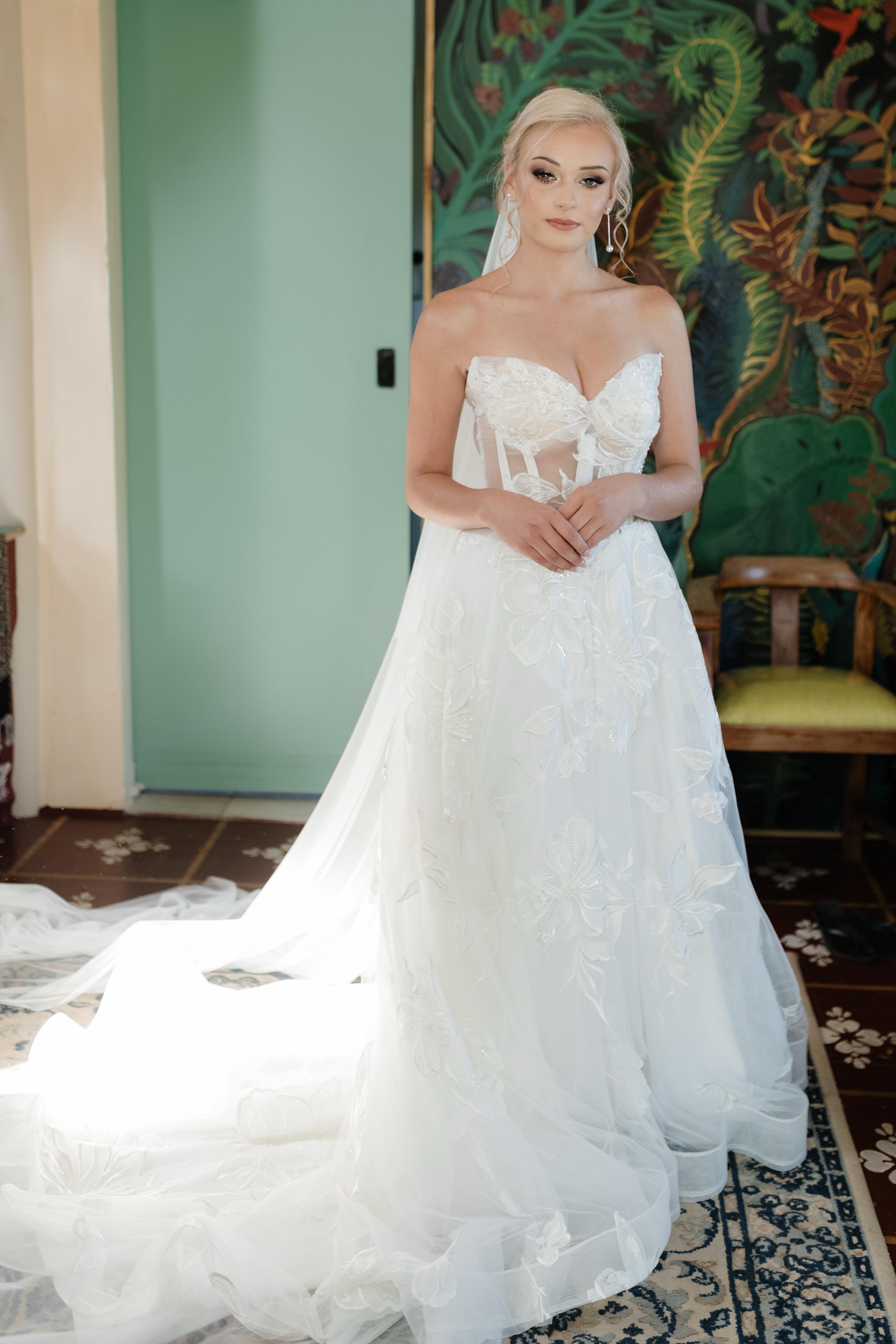 ANke Anke – Winter White A-Line Princess Gown with Bold Floral Lace & Sheer Bodice  The Anke gown is a striking and romantic choice for the bride who wants to make a fairytale statement with modern edge. Crafted from soft tulle and bold floral lace, this A-line princess silhouette offers both volume and ethereal grace, perfect for a grand entrance.