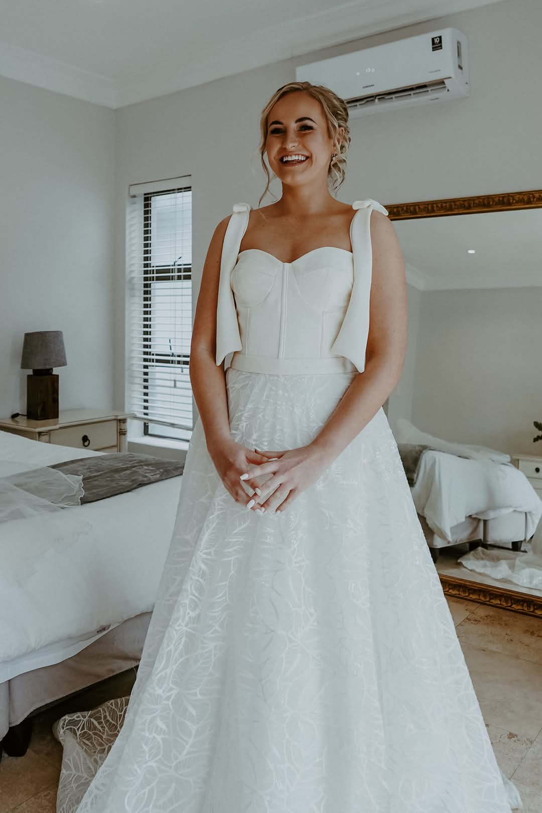 DOMINIQUE Ivory Crepe & Lace A-Line Bridal Gown with Bow-Tie Straps  Designed for the modern romantic, this elegant bridal gown is a perfect fusion of classic bridal elegance and contemporary charm. Crafted from luxurious ivory crepe, satin, and lace, the gown features a structured corset bodice, providing a flattering, form-enhancing fit that beautifully accentuates the waistline.  The delicate bow-tie straps add a playful yet sophisticated touch, enhancing the gown’s femininity. Flowing effortlessly into a full-flare A-line silhouette, the lace skirt exudes romance and grace, with intricate lace detailing throughout. A wide horsehair hemline adds volume and definition, creating a dramatic, captivating movement with every step.