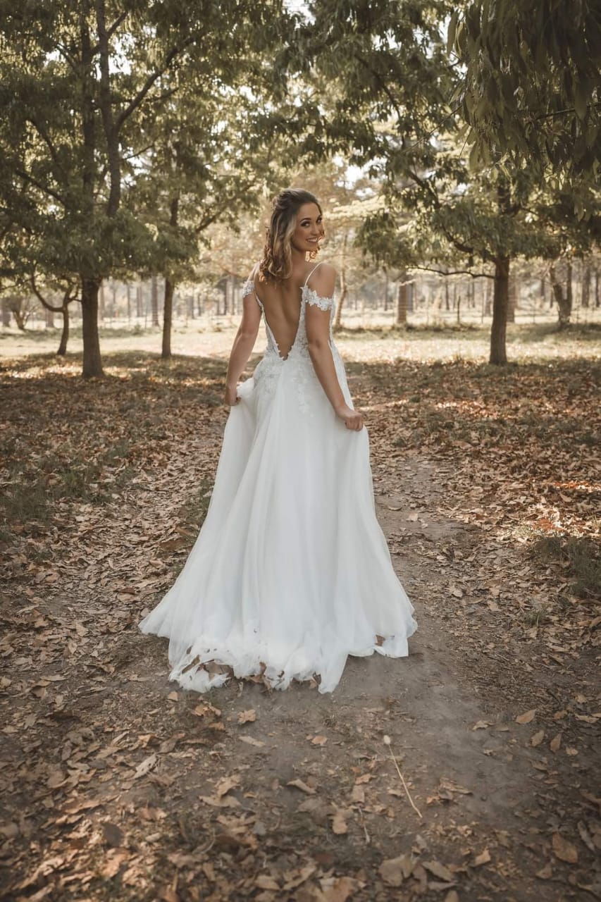 MARELIZE This enchanting bridal gown features a deep plunging V-shaped neckline crafted from luxurious off-white Chantilly lace and adorned with delicate embroidered lace details. The bodice is supported by thin, elegant straps and complemented by gracefully draped off-the-shoulder lace straps for a romantic touch. The gown flows into a stunning A-line tulle skirt, designed with a daring high slit that adds a contemporary edge to its timeless elegance. The back showcases a dramatic low V-shaped design, ensuring breathtaking views from every angle.