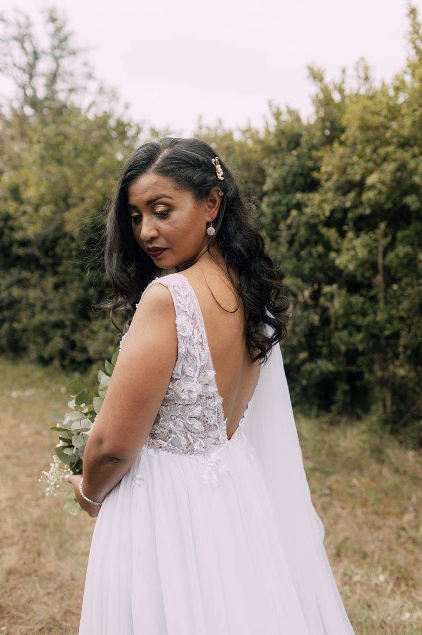 anjee A breathtaking white bridal gown featuring a sheer lace bodice with a daring deep V-neckline, elegantly adorned with intricate 3D floral lace appliqués that add dimension and a touch of nature-inspired beauty. The A-line tulle skirt flows softly from the waist, creating a romantic and ethereal silhouette. At the back, the gown showcases a low V-back bodice, offering a hint of allure while maintaining elegance. The gown is finished with a short, graceful train that gently trails behind, completing this enchanting design with a sense of understated sophistication.